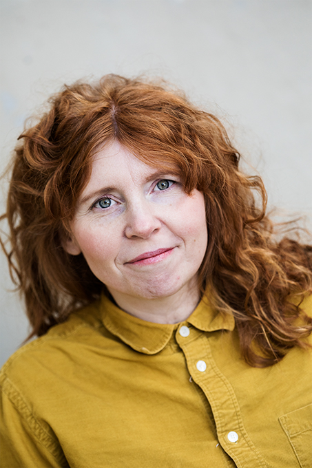 Portrait picture of dancer Emilia Wärff. Emilia has long red curly hair and a mustard yellow shirt. Photo: Polina Ulianova