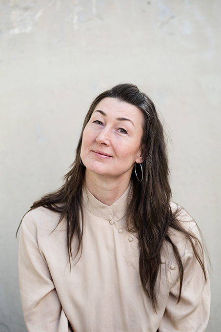 Porträttbild av Liselotte Reivén, administratör för Kulturklustret. Liselotte har långt brunt hår, stora silverringar i öronen och en beige blus. Foto: Polina Ulianova
