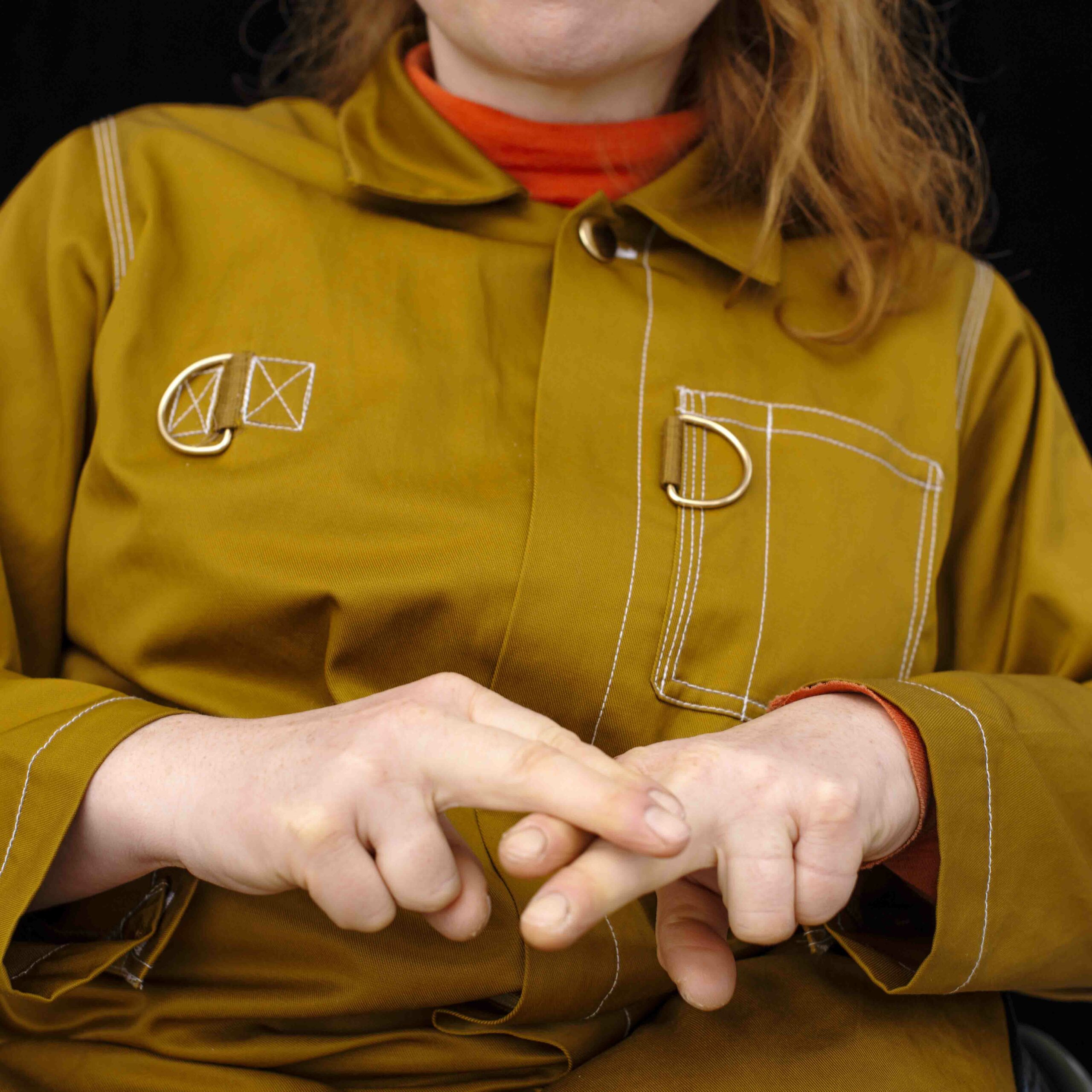 The image depicts a person wearing a mustard-yellow dress over a bright red sweater. They sign with their hands. Photo: Lars Dyrendom